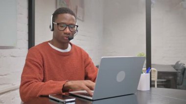 Kulaklıklı Afrikalı Amerikalı Çağrı Merkezi 'nde dizüstü bilgisayarda çalışıyor.