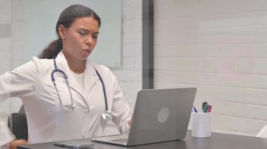 Klinikte dizüstü bilgisayar kullanırken sırt ağrısı olan Afrikalı genç bir doktor.