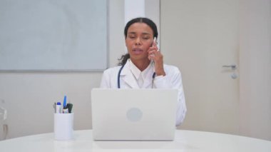 Bilgisayarda çalışırken telefonda konuşan Afrikalı Doktor