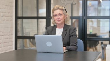 Ofiste dizüstü bilgisayarla çalışırken Yaşlı İş Kadını Kameraya Bakıyor