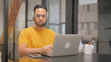 Bilgisayarda çalışırken Kameraya Bakan Kulaklıklı Yaratıcı Karışık Yarış Adamı