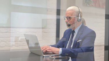 Kulaklıklı kıdemli iş adamı laptopta çalışıyor.