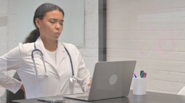 Klinikte dizüstü bilgisayar kullanırken sırt ağrısı olan Afrikalı genç bir doktor.