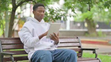 Açık havada otururken dijital tablet kullanan sıradan bir Afrikalı Amerikalı.