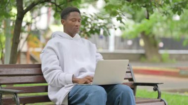 Park 'ta dizüstü bilgisayar kullanırken sırt ağrısı çeken sıradan bir Afrikalı Amerikalı.