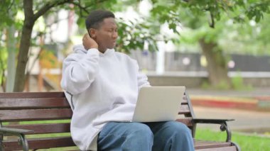 Park 'ta dizüstü bilgisayar kullanırken boynu ağrıyan sıradan bir Afrikalı Amerikalı.