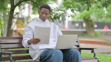 Günlük Afrikalı Amerikalı Adam Park 'ta dizüstü bilgisayarlı belgeleri inceliyor