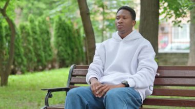 Bankta oturan boynu ağrıyan genç Afrikalı adam.