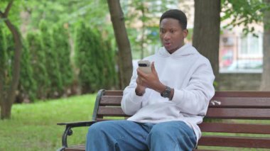 Genç Afrikalı Kayıplarla Yüzleşen Adam Akıllı Telefon 'da, Açık Hava Bankında Oturuyor