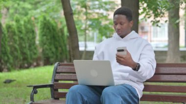 Açık havada otururken akıllı telefon ve dizüstü bilgisayar kullanan genç Afrikalı adam