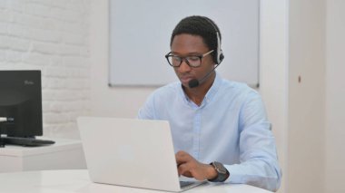 Kulaklıklı genç Afrikalı İşadamı Laptop üzerinde çalışıyor