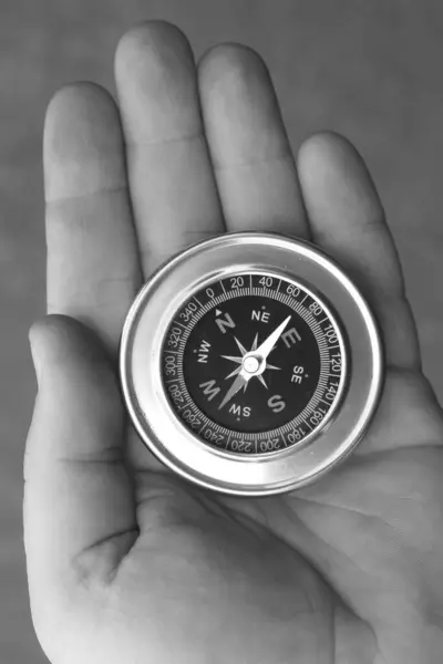 black and white photo of round compass in hand as symbol of tourism with compass, travel with compass and outdoor activities with compass