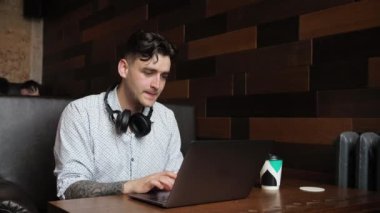 Serbest çalışan genç bir iş adamı esmer bir adam bir laptopun arkasında bir kafede oturuyor. Çalıştım, ders çalıştım, kahve içtim. Kulaklıkla müzik dinlemek