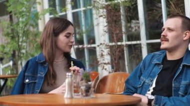 Genç bir çift. Denim giysileri. Eski bir restoranda randevuda, dışarıda. Konuşuyorlar. Sallanıyorlar.