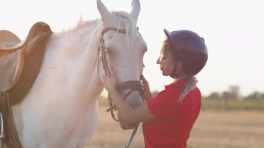 Kırmızı üniformalı bir kadın beyaz bir atı okşar, kucaklar ve okşar. Orta boy..