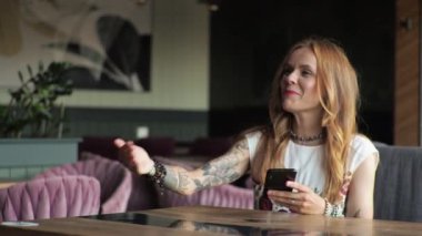 Günlük kıyafetli genç bir kadın bir kafede pencerenin kenarında oturup kahve içiyor. Garson kahveyi getirir ve götürür..