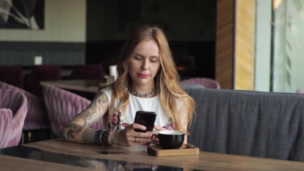 Egy Alkalmi Ruhás Fiatal Ablaknál Egy Kávézóban Kávézik Nézem Telefont — Stock videók