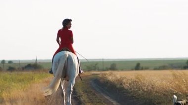 Kırmızı üniformalı bir kadın saman tarlasında beyaz bir atın üzerinde yürüyor. Geniş açı. Kameradan uzaklaşır. Arkadan bak..