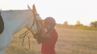 Kırmızı üniformalı bir kadın beyaz bir atı okşar, kucaklar ve okşar. Orta boy..