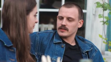 Genç bir çift. Denim giysileri. Eski bir restoranda randevuda, dışarıda. Konuşuyorlar..