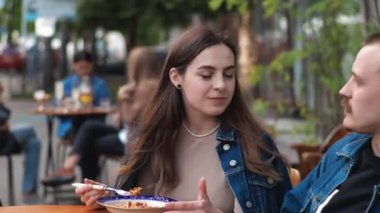 Genç bir çift. Denim giysileri. Eski bir restoranda randevuda, dışarıda. Konuşuyorlar..