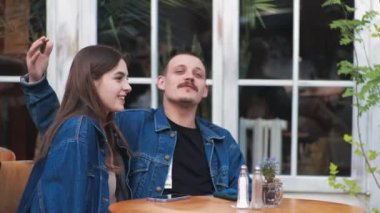 Genç bir çift. Denim giysileri. Eski bir restoranda randevuda, dışarıda. Konuşuyorlar. Sallanıyorlar.