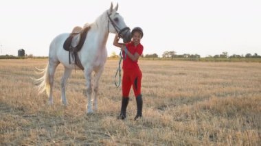Kırmızı üniformalı bir kadın beyaz bir atı okşar, kucaklar ve okşar. Geniş açı.