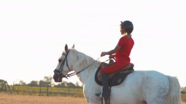 Kırmızı üniformalı bir kadın saman tarlasında beyaz bir atın üzerinde yürüyor. Orta boy..