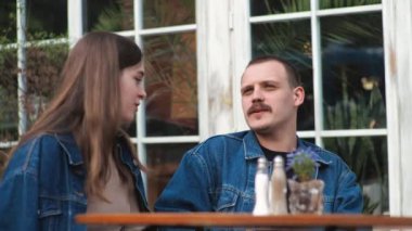 Genç bir çift. Denim giysileri. Eski bir restoranda randevuda, dışarıda. Konuşuyorlar..