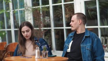 Genç bir çift. Denim giysileri. Eski bir restoranda randevuda, dışarıda. Konuşuyorlar..