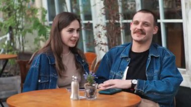 Genç bir çift. Denim giysileri. Eski bir restoranda randevuda, dışarıda. Konuşuyorlar. Sallanıyorlar.