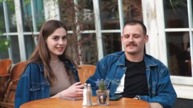 Genç bir çift. Denim giysileri. Eski bir restoranda randevuda, dışarıda. Konuşuyorlar. Sallanıyorlar.