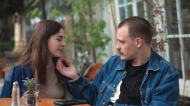 Genç bir çift. Denim giysileri. Eski bir restoranda randevuda, dışarıda. Konuşuyorlar. Sallanıyorlar.