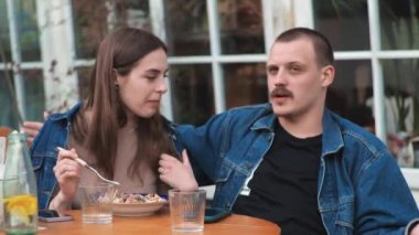 Genç bir çift. Denim giysileri. Eski bir restoranda randevuda, dışarıda. Konuşuyorlar..