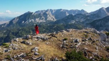 Dağlarda dans eden kırmızı elbiseli genç kadın doğanın ve özgürlüğün tadını çıkarıyor. Durmitor, Karadağ seyahati.
