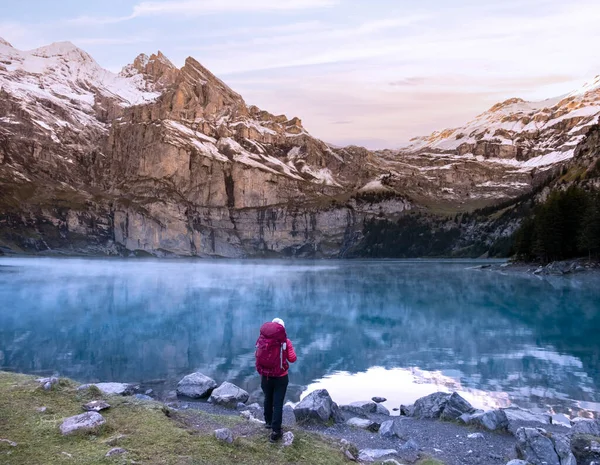 背景には曇り空の山の峰がある日の出にスイスの山の湖の近くにリュックを持つハイカーの女の子 スイスのOeschinensee湖 Alps — ストック写真