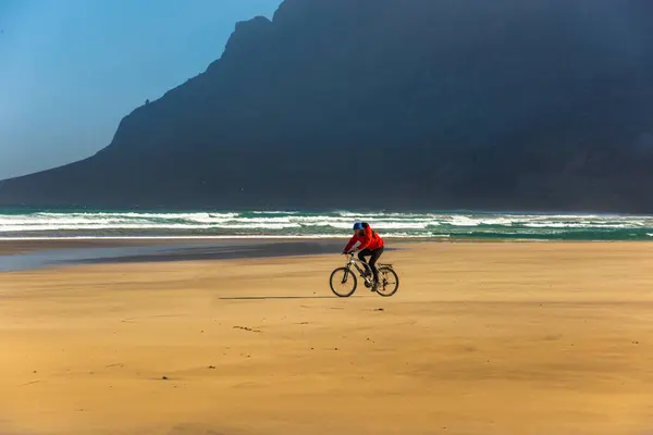 Sporty young man ride bicycle on sand Famara beach. Lanzarote Canary Island