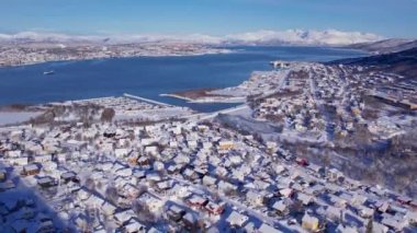 Norveç 'in Tromso kasabasının fiyort ve köprüsündeki karlı evlerin hava günbatımı manzarası. Güneşli kış havası
