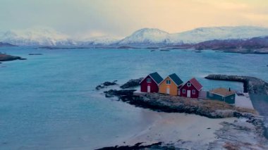 Norveç 'in Sommaroy adasında, kar kaplı dağ zeminli küçük geleneksel rorbu balıkçı kulübelerinin havası
