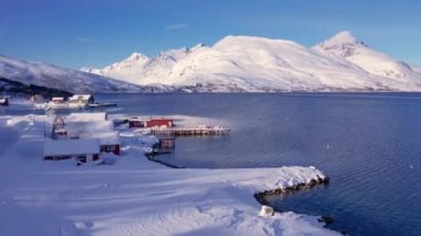 Norveç 'in kışın kıyı şeridi üzerindeki balıkçı köyü karla kaplıydı. Kasabanın çevresi Tromso. Kuzey dağlarının panoramik manzarası, evler, rorbu, botlar ve okyanus. Troms county, Fjordgard