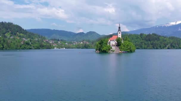 湖の中心にあるマリアの仮定の教会の空想的な眺め スロベニアのブレッド湖で小さな島を飛び回る 暖かい夏の日の太陽 — ストック動画