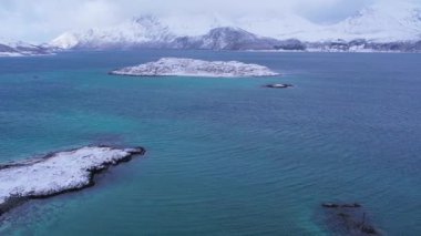 Norveç 'in Sommaroy adasında, güneşli kış mevsiminde, karla kaplı dağ zeminli bir kumsal çevresindeki hava manzarası