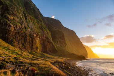 Volkanik kaya kayalıkları güneş ışığında Achadas da Cruz. Atlantik Okyanusu dalgaları. Portekiz, Madeira tatil köyünün güzel gün batımı deniz manzarası
