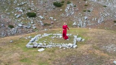 Dağlarda dans eden kırmızı elbiseli genç kadın doğanın ve özgürlüğün tadını çıkarıyor. Durmitor, Karadağ seyahati.