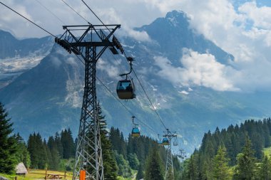 İsviçre Alplerinde kablolu bir araba. Jungfrau, Grindelwald 'dan Gondol. Karla kaplı arka planlı yaz Alp manzarası. Nakliye turistleri yokuş yukarı