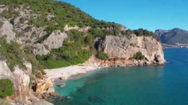 Sardegna 'daki Cala Fuili plajında hava aracı görüntüsü. Sardunya adasında yeşil dağlarla çevrili ılık turkuaz deniz ve küçük plaj.