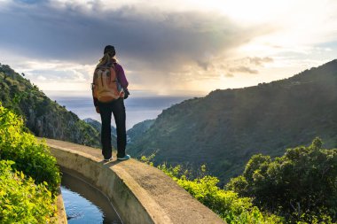 Portekiz 'in Madeira adasında Levada do Norte' de bir turist. Levada sulama kanalı. Madeira 'da yürüyüş. Levada 'nın yanındaki dar yol. Arkaplanda yeşil dağlar ve okyanus.