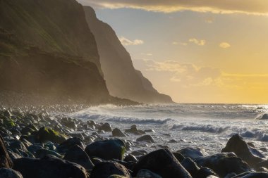 Volkanik kaya kayalıkları güneş ışığında Achadas da Cruz. Atlantik Okyanusu dalgaları. Portekiz, Madeira tatil köyünün güzel gün batımı deniz manzarası