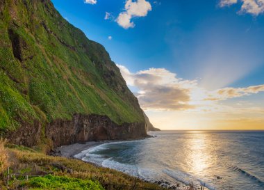 Volkanik kaya kayalıkları güneş ışığında Achadas da Cruz. Atlantik Okyanusu dalgaları. Portekiz, Madeira tatil köyünün güzel gün batımı deniz manzarası