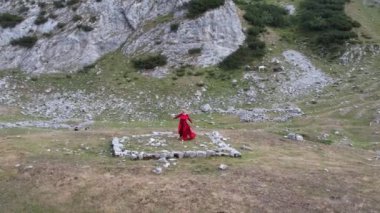 Dağlarda dans eden kırmızı elbiseli genç kadın doğanın ve özgürlüğün tadını çıkarıyor. Durmitor, Karadağ seyahati.